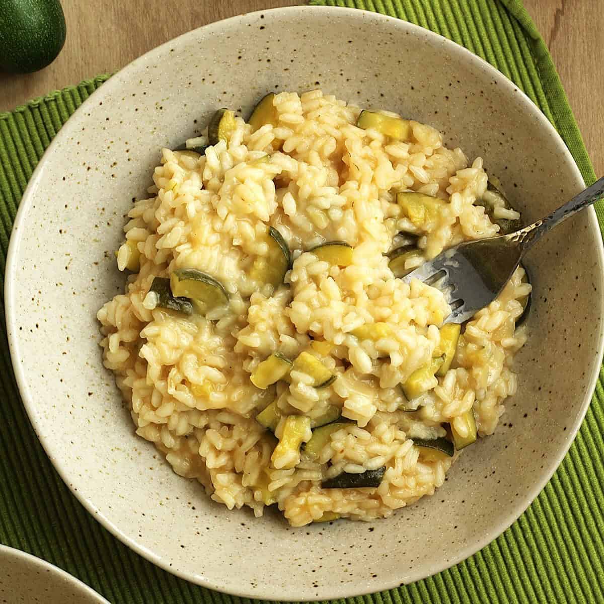 Risotto with zucchini and scamorza cheese in bowl with fork in it.