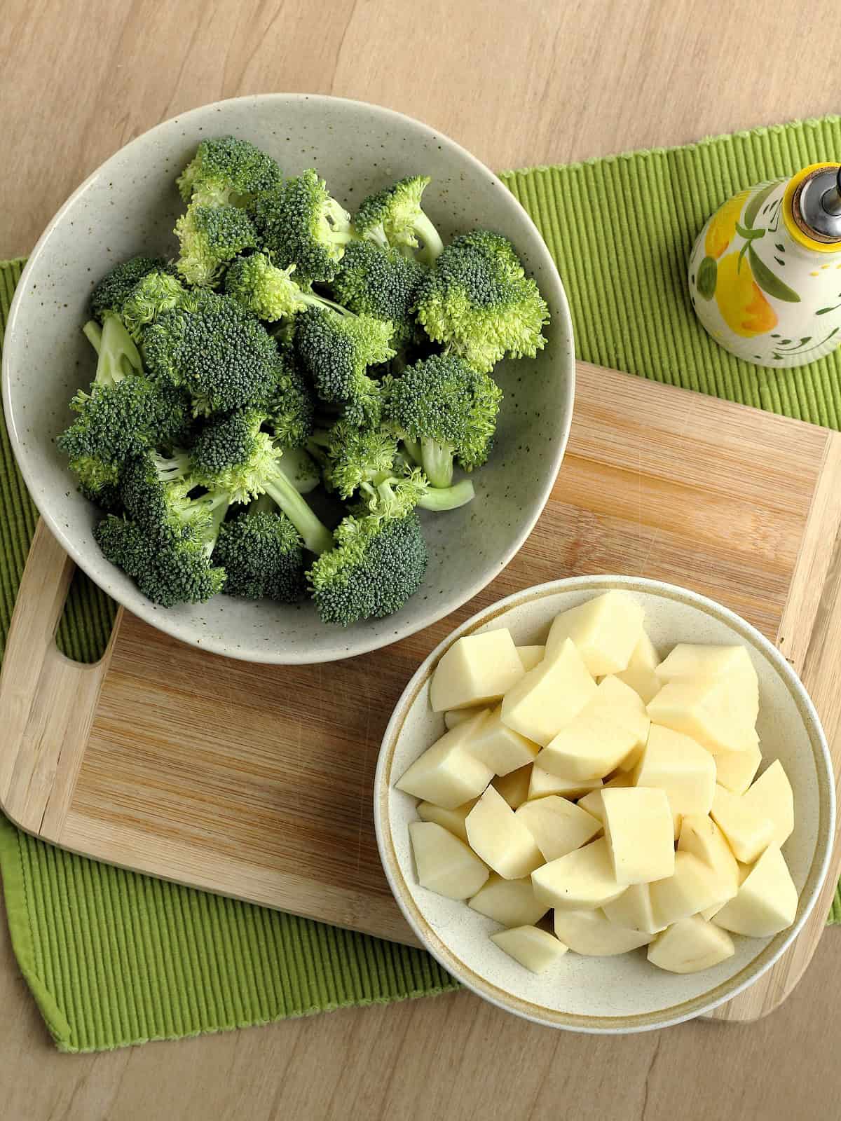 Broccoli florets in bowl next to cubed potatoes in bowl for broccoli patties.