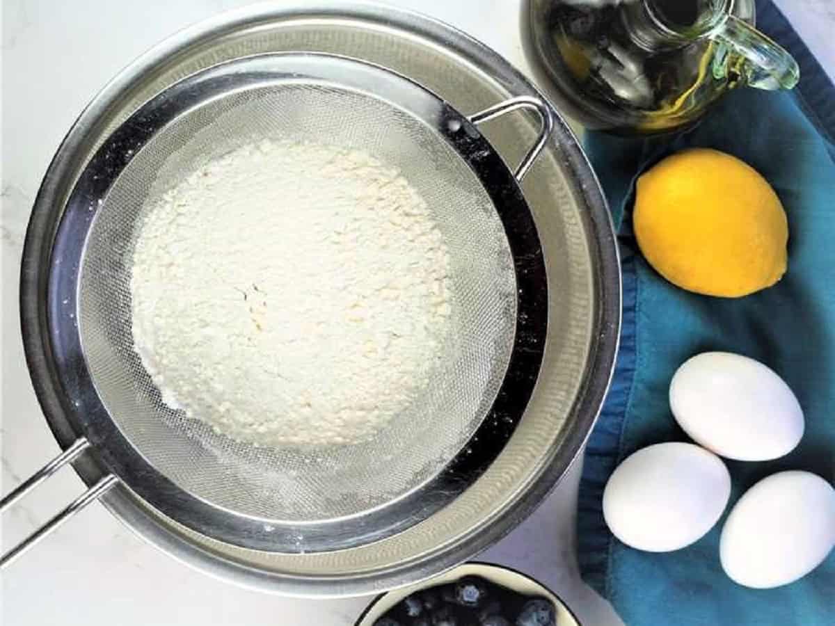 Flour sifted over bowl next to eggs and lemon.