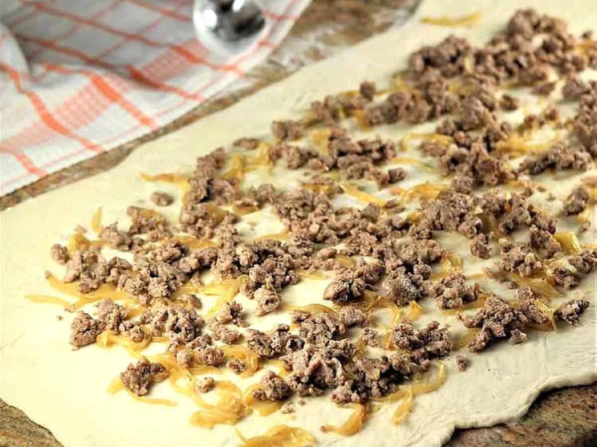 Sautéed onions and sausage without casing spread out over flattened bignolati dough.