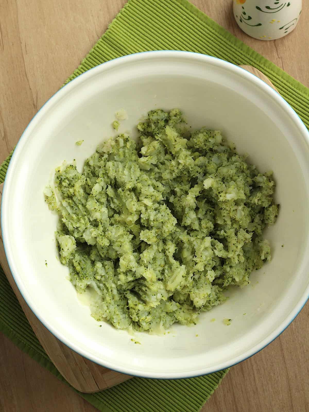 Mashed broccoli and potatoes in bowl for broccoli cakes recipe.