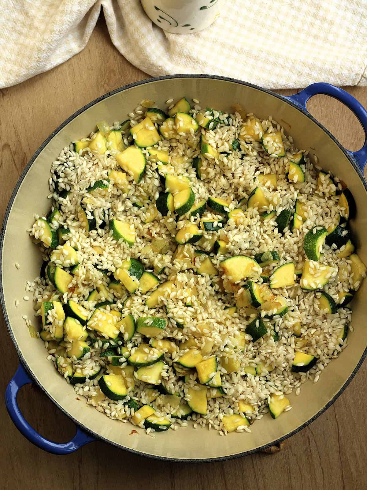 Arborio rice stirred into zucchini in sauce pan.