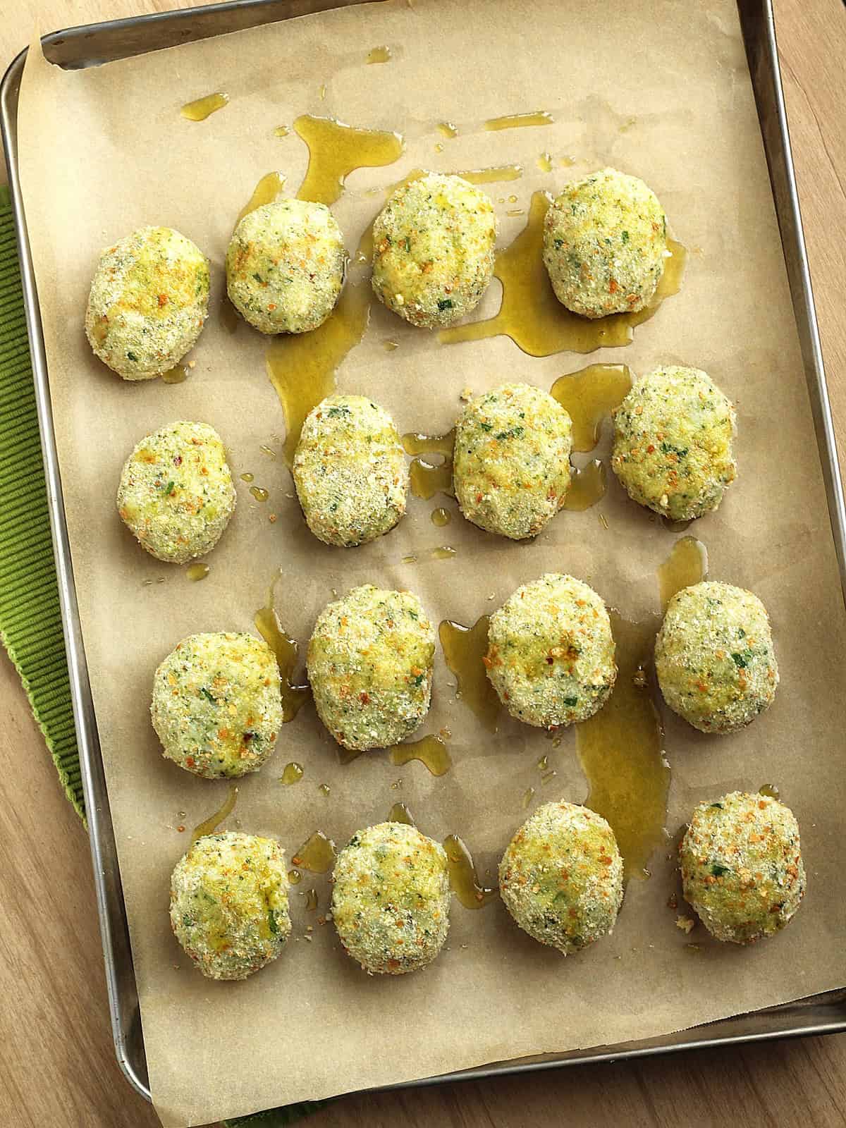 Potato broccoli patties on baking sheet topped with olive oil.