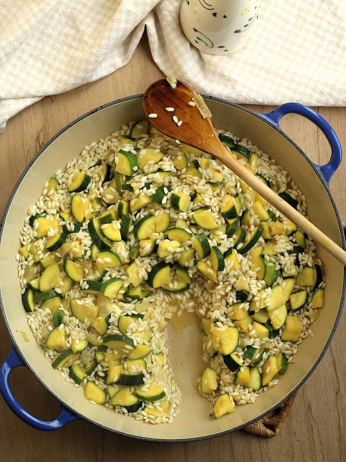 Zucchini risotto stirred with wooden spoon in sauce pan.