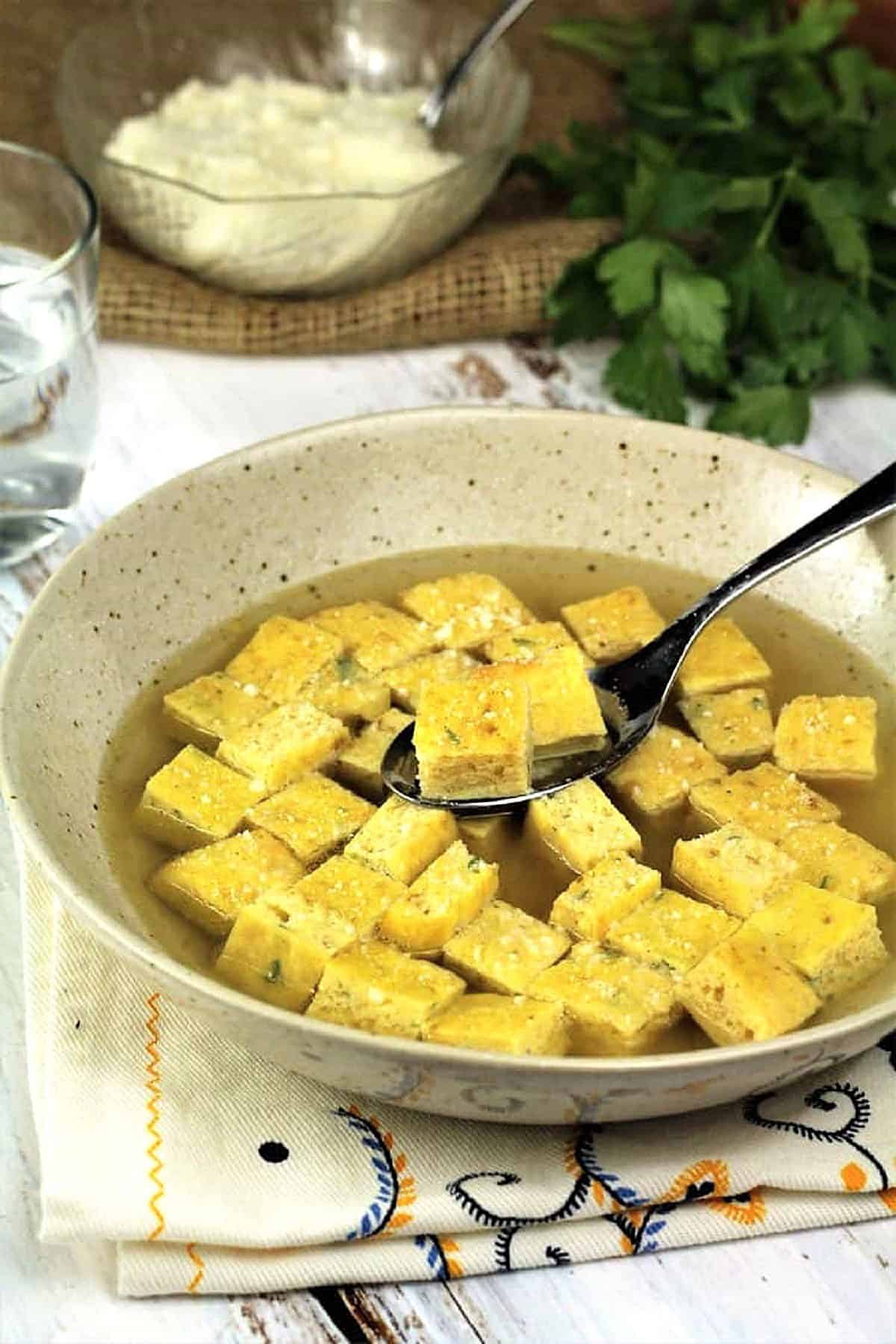 Bowl of frittata soup (zuppa imperiale) with spoon in it.