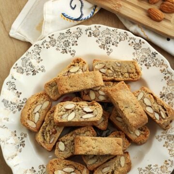 Sicilian quaresimali biscotti with almonds on plate surrounded by orange wedges and almonds.