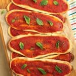 Lingue di pizza topped with basil piled on wood board.