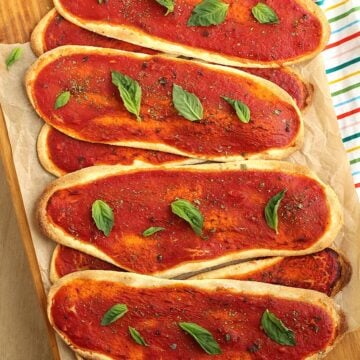 Lingue di pizza topped with basil piled on wood board.