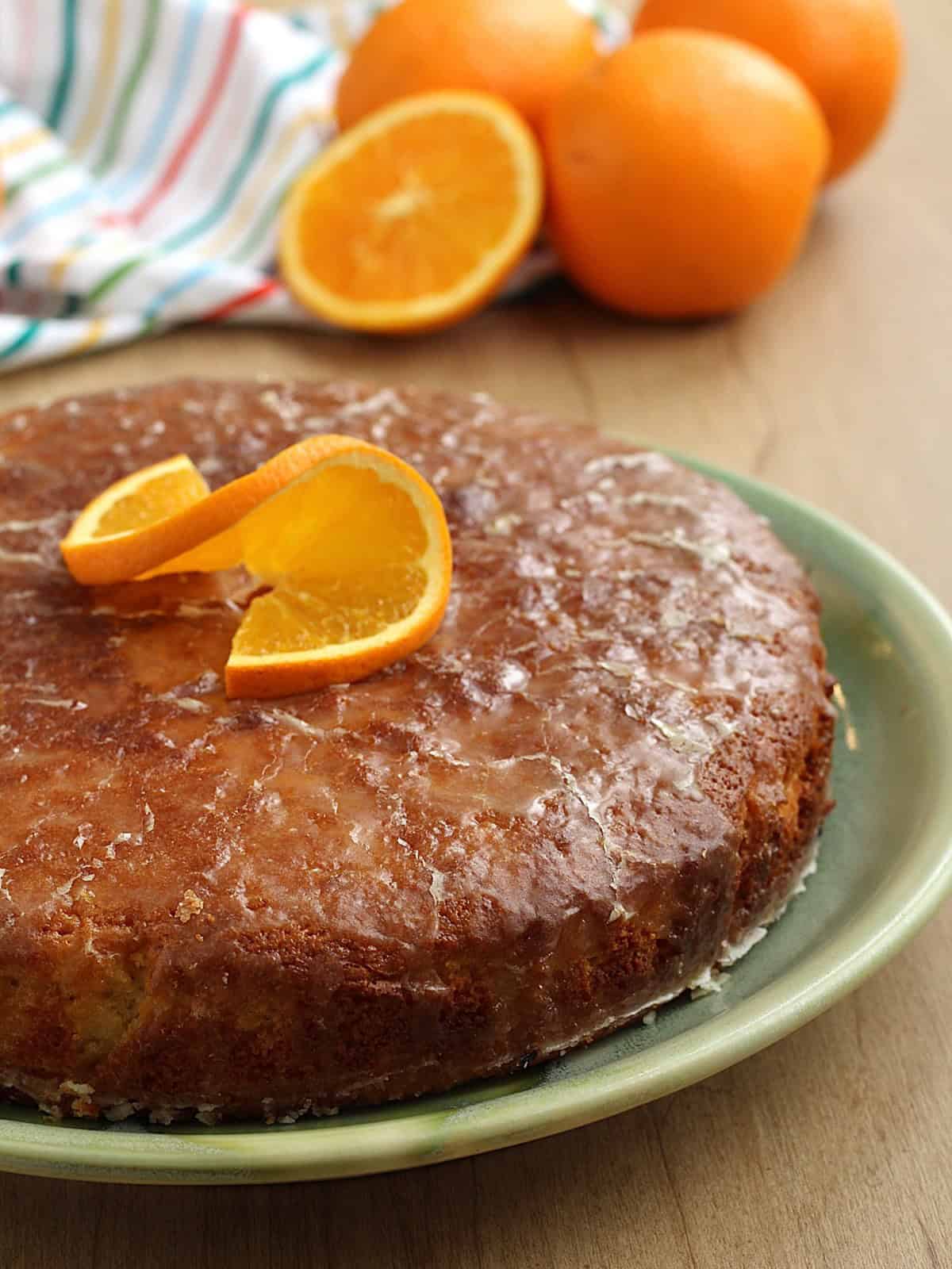 Sicilian orange cake topped with glaze and orange slice on plate.