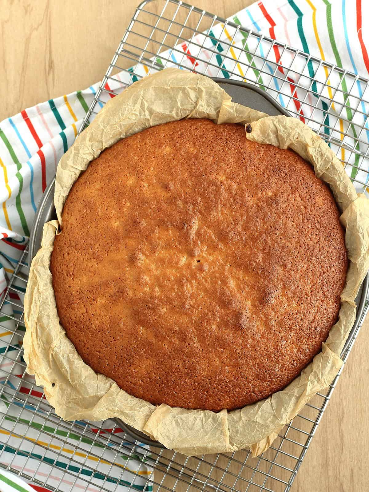 Baked Sicilian whole orange cake in cake pan resting on wire rack.