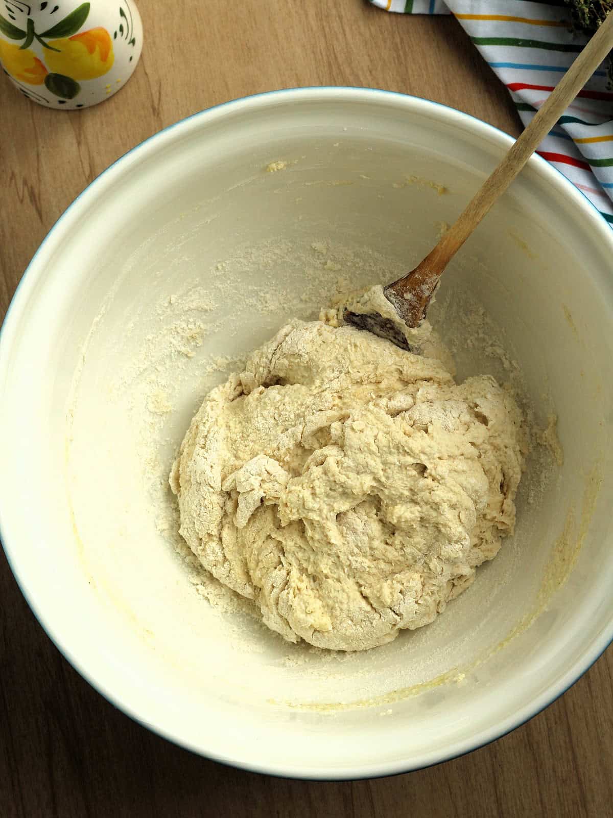 Shaggy lingue di pizza dough stirred in bowl with wooden spoon.