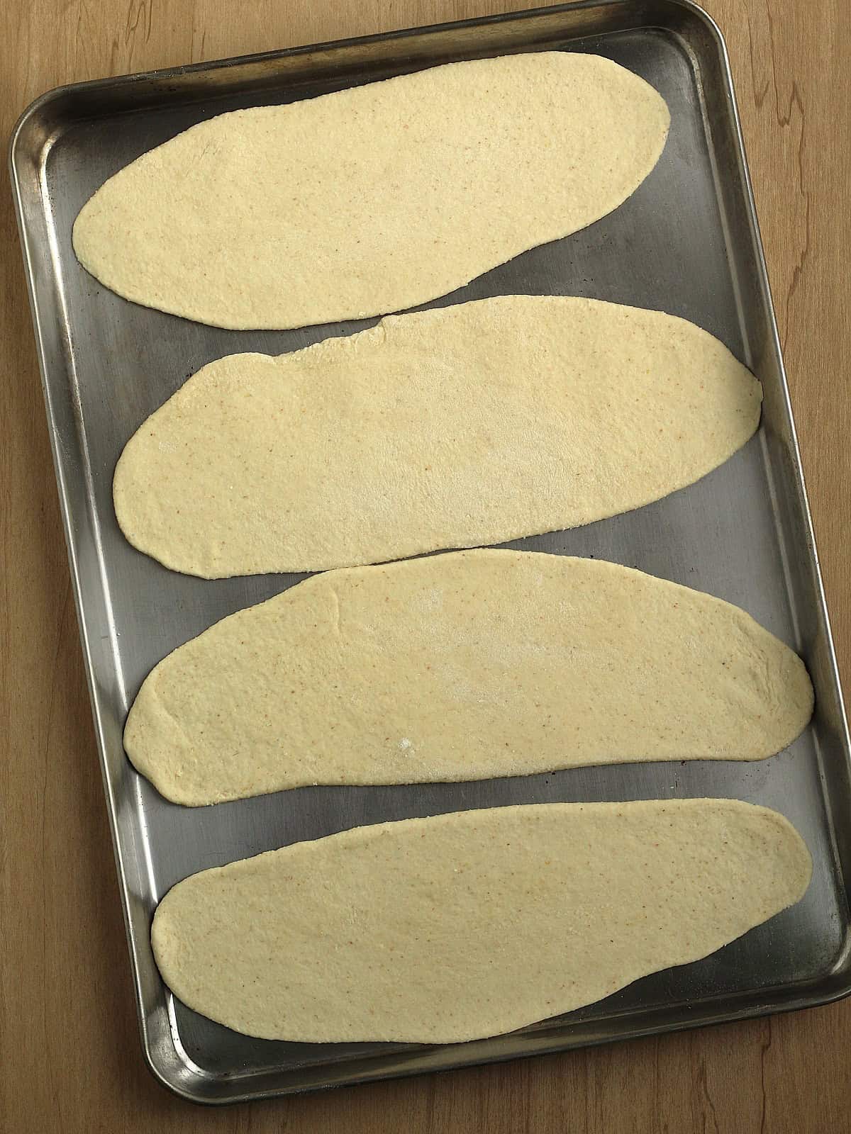Pizza dough flattened into oval shapes on baking sheet.