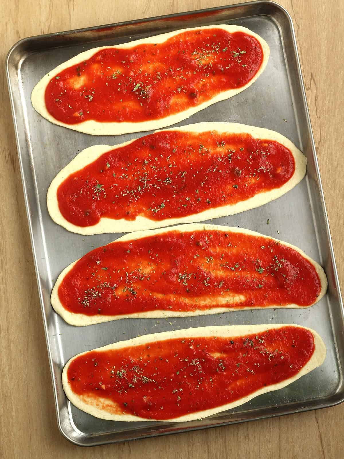 Lingue di pizza topped with tomato sauce on baking sheet.