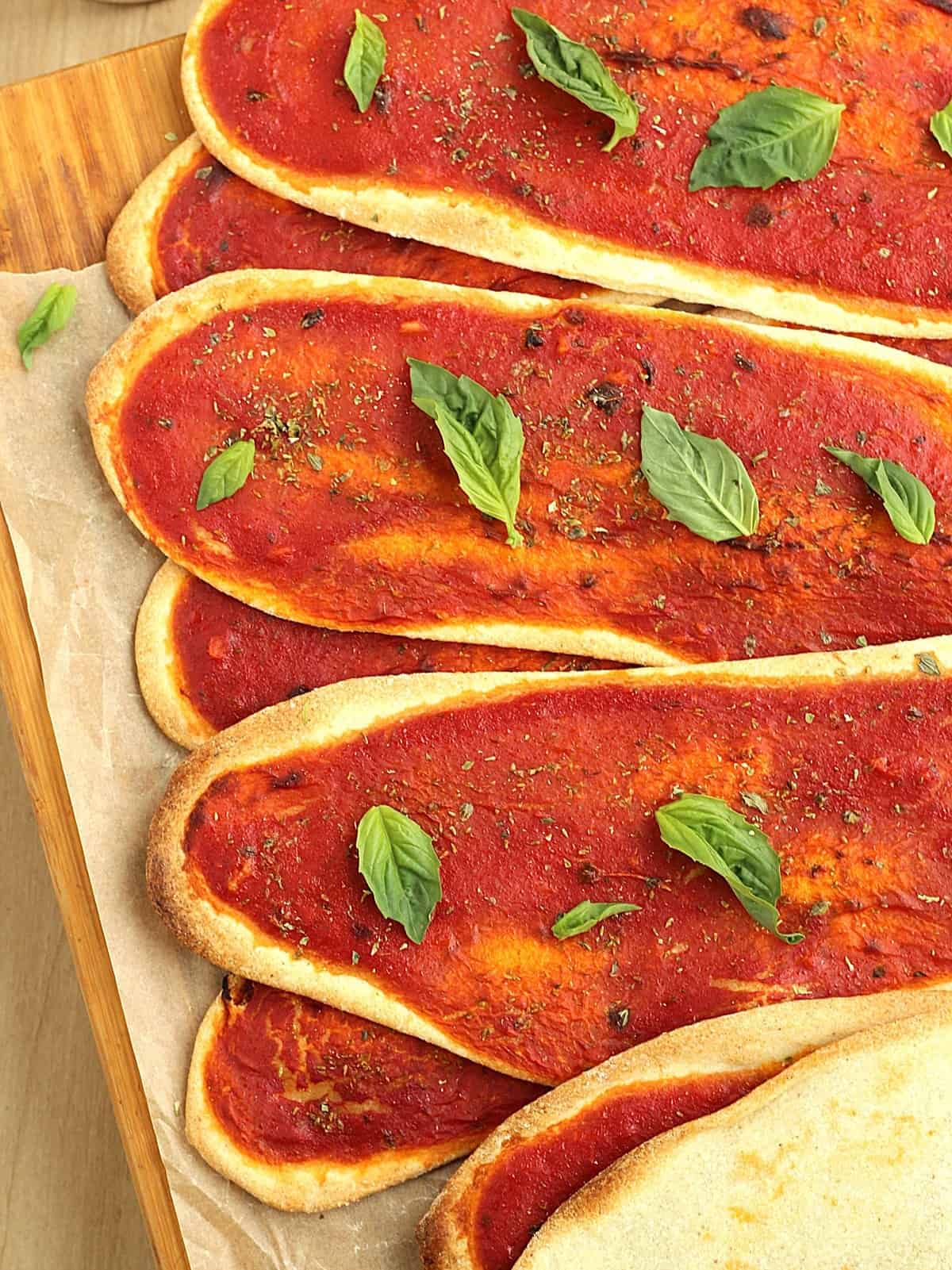 Thin, crispy lingue di pizza with tomato sauce piled on wood board.