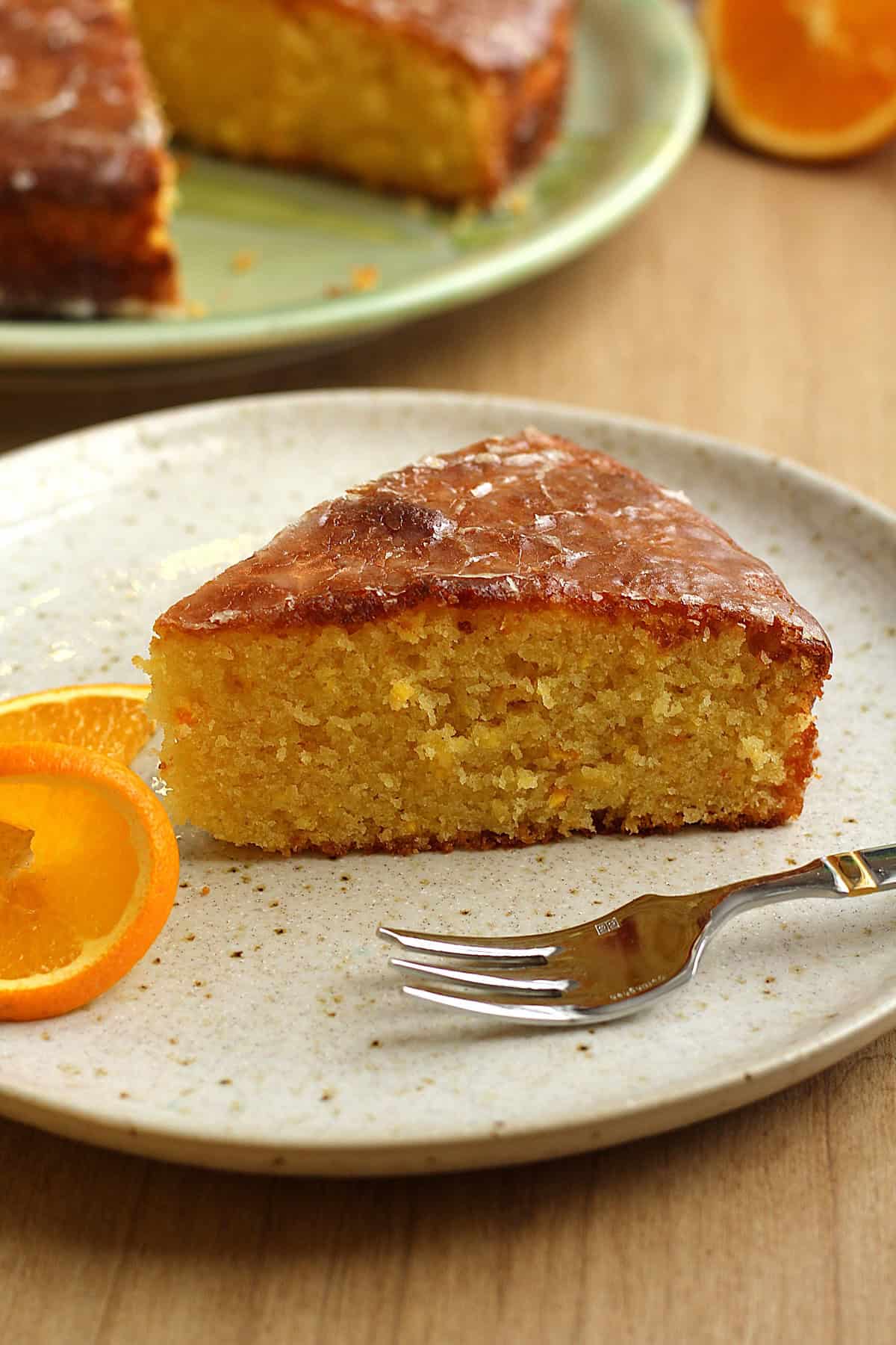 Sicilian whole orange cake slice on plate with fork and orange slice.
