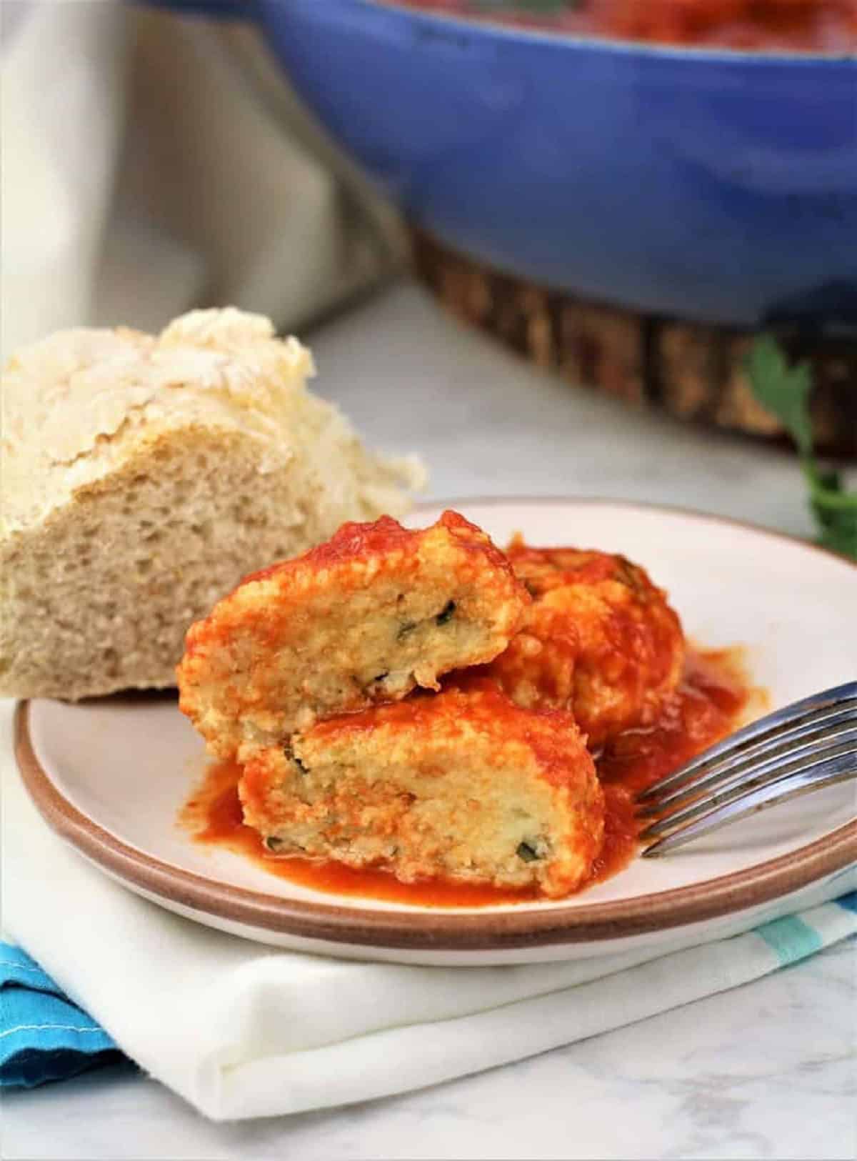 Bread meatballs in tomato sauce on plate with fork next to slice of bread.