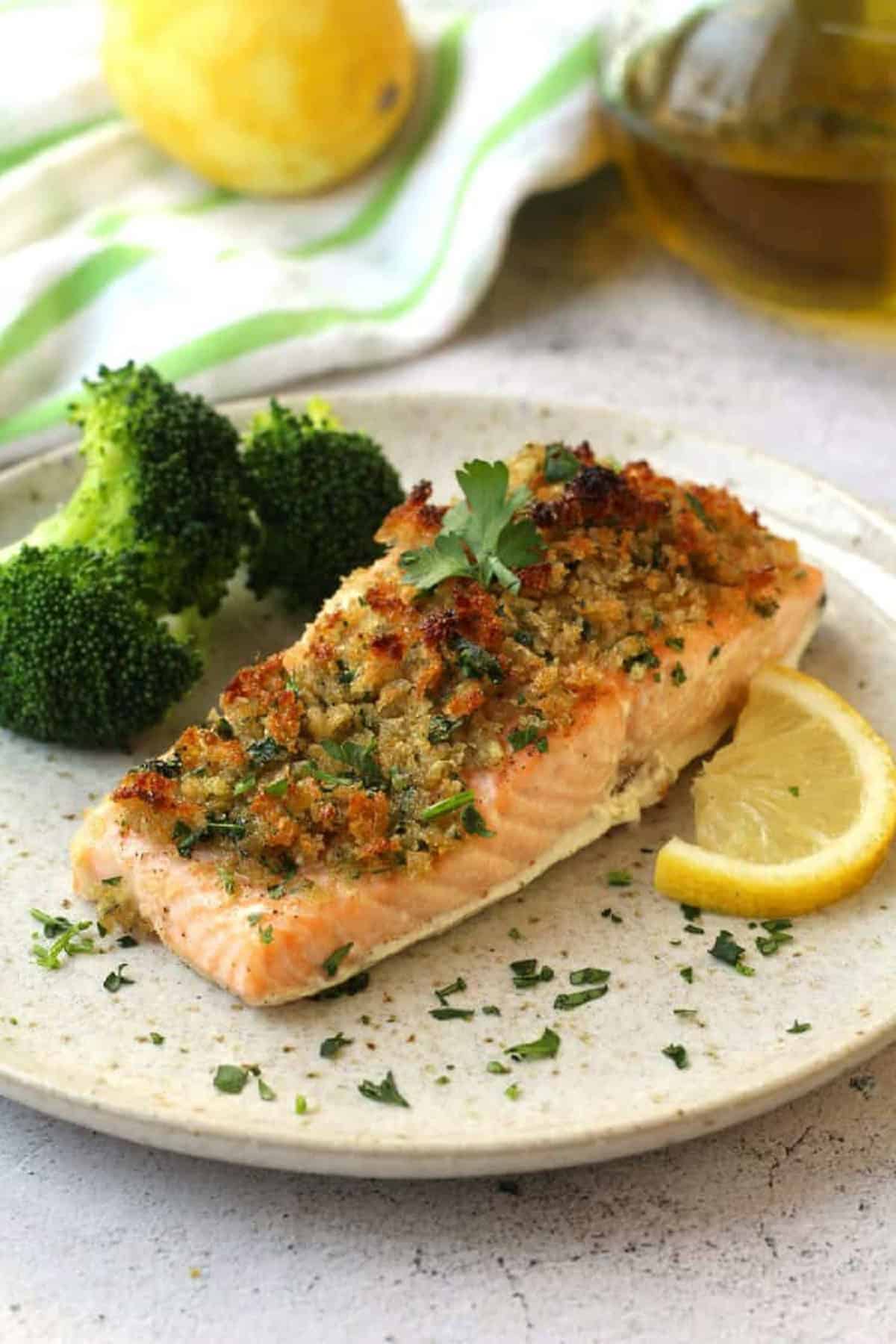 Salmond fillet with crispy breadcrumb topping plated with broccoli and lemon wedge.