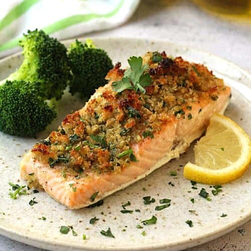 Baked salmon with crispy breadcrumbs plated with broccoli and lemon wedge.