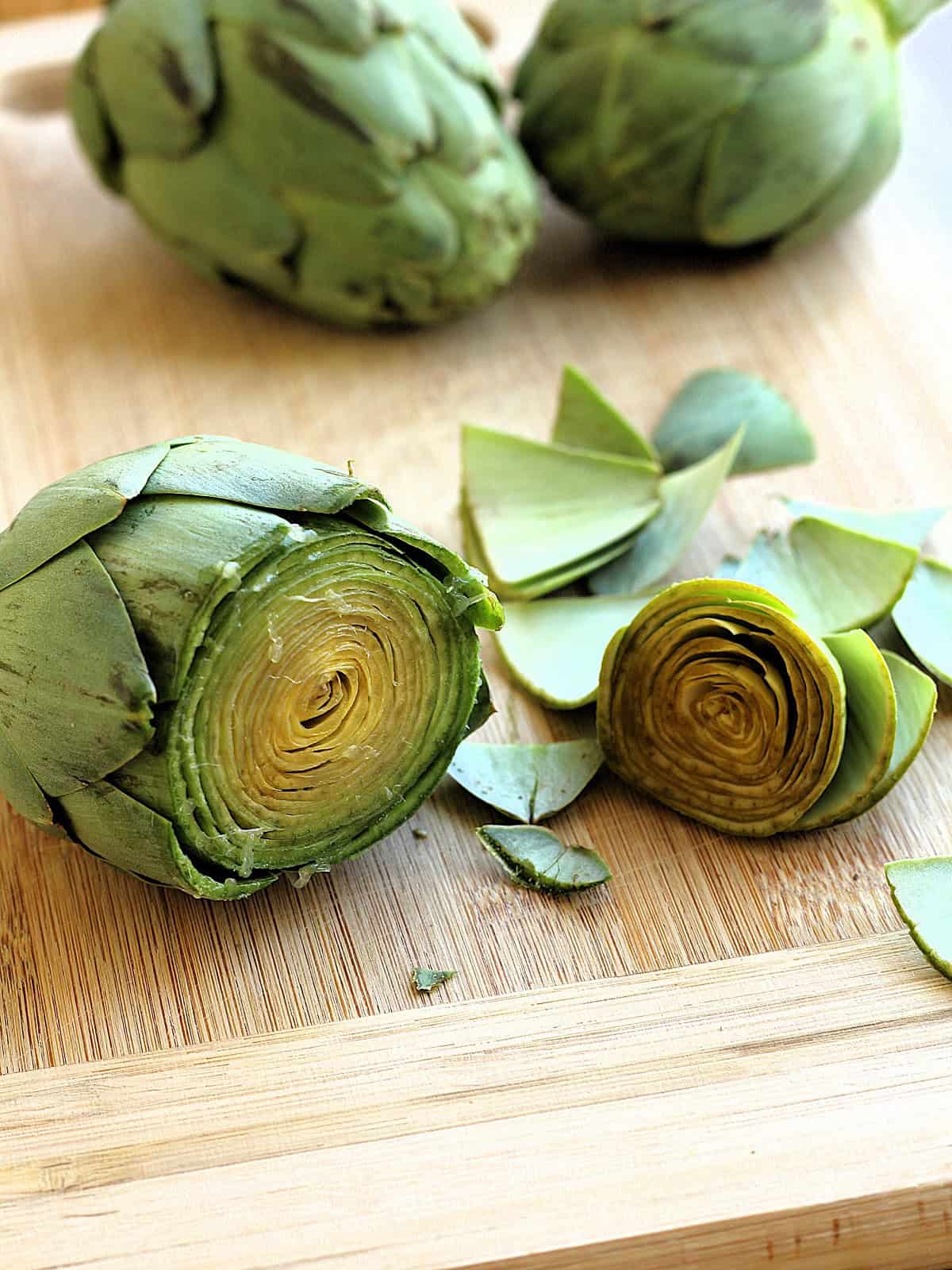 Artichoke  with the top third cut off on wood board.