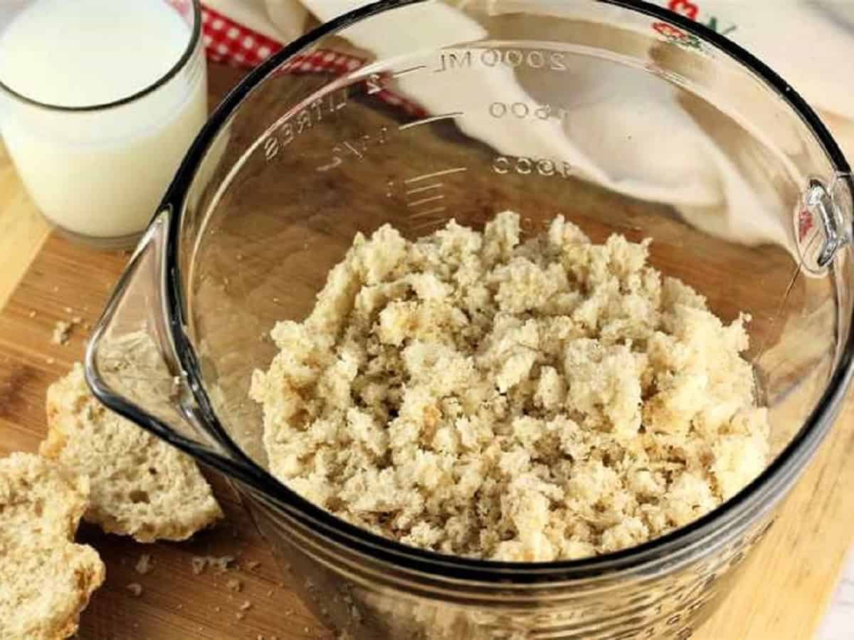 Bread torn into small pieces in bowl with glass of milk next to it.