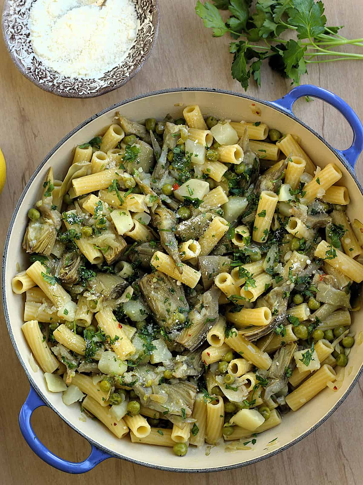 Large skillet filled with pasta, artichokes, peas and potatoes with bowl of grated cheese for serving on the side.