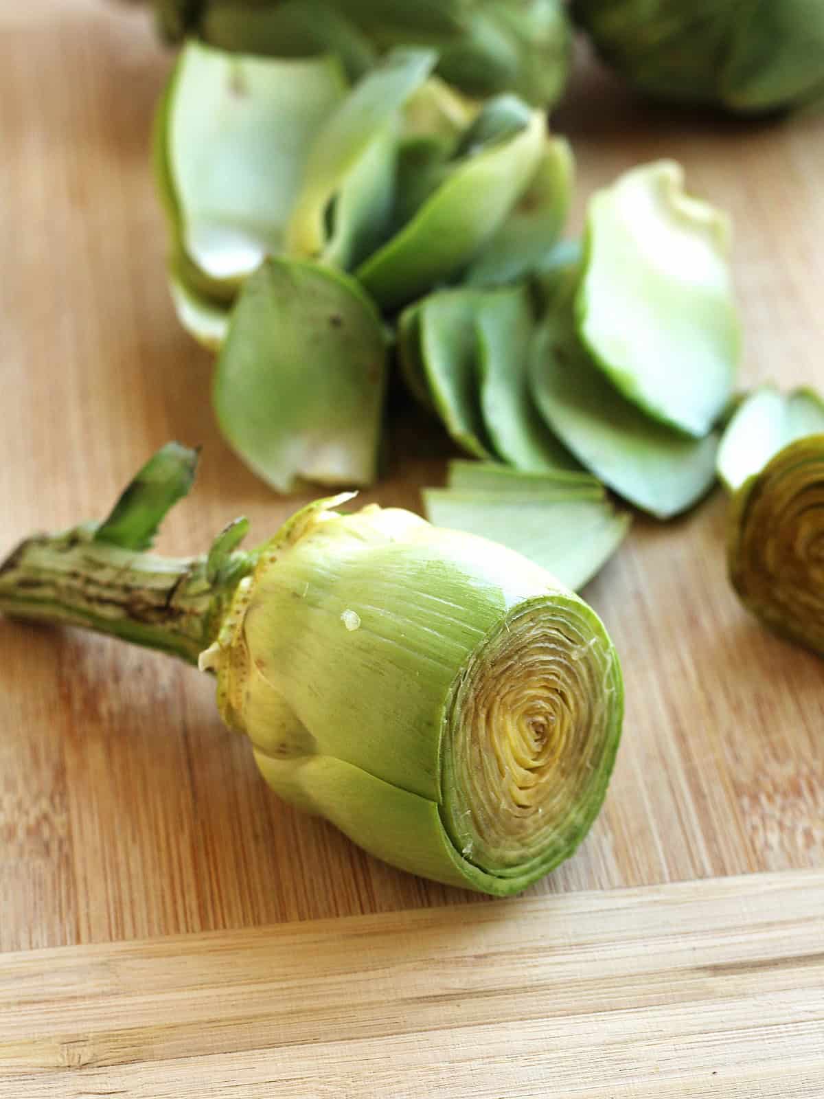 Tough outer leaves of artichokes are removed to reveal pale green tender part of the artichoke.