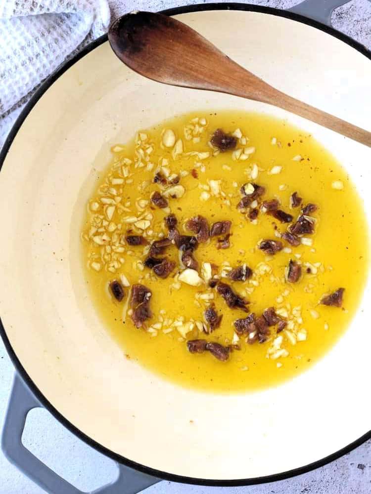 Garlic and anchovies in olive oil in skillet for anchovy pasta recipe.