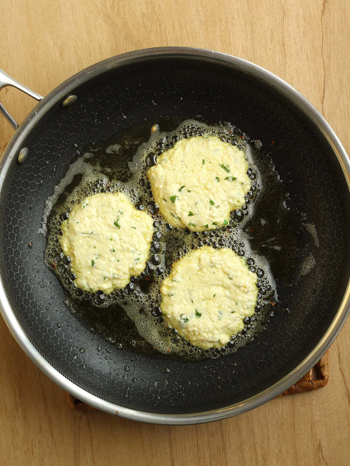 Ricotta cheese fritters frying in skillet coated with olive oil.