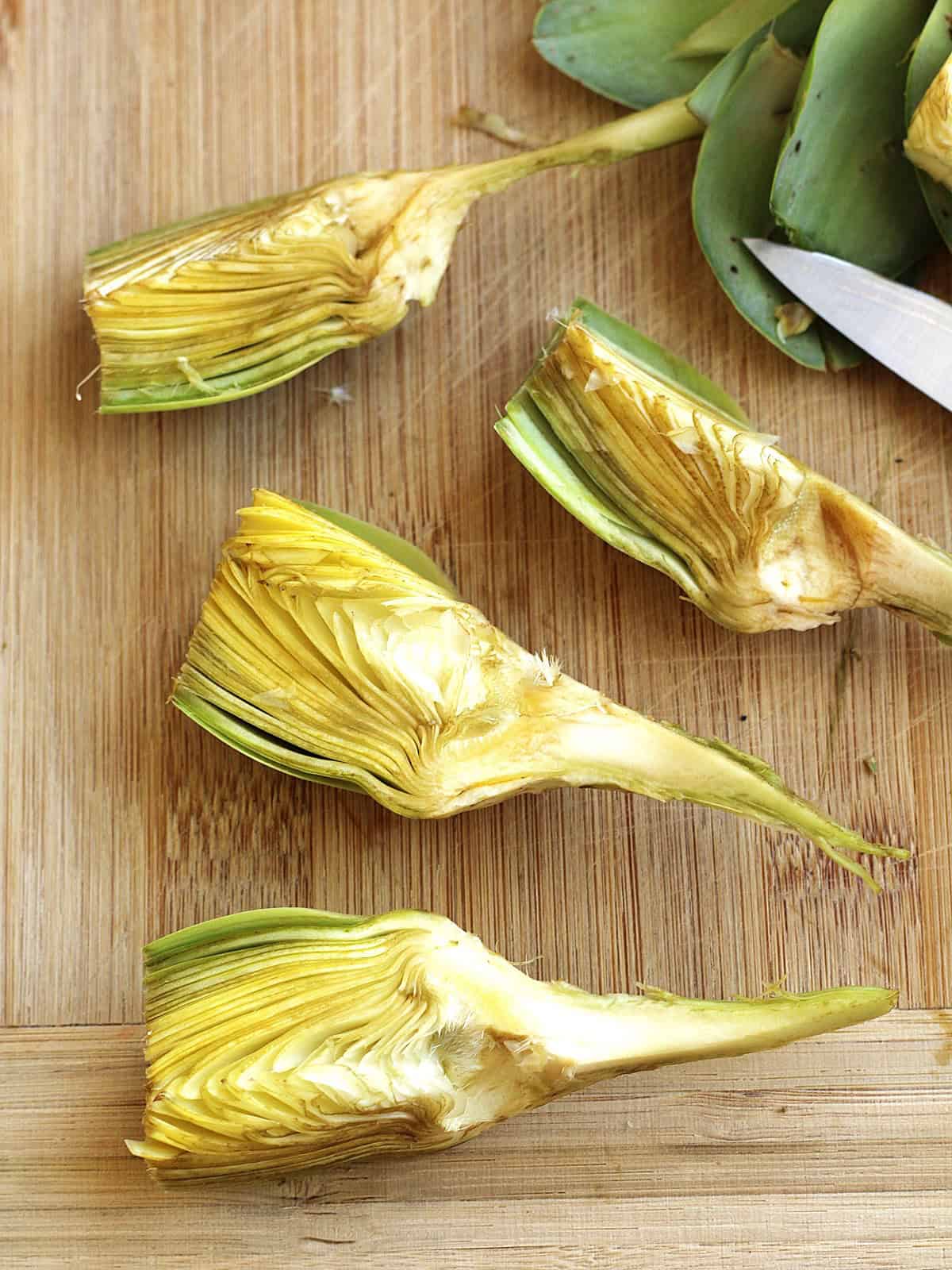 Cleaned artichoke cut into quarters on wood board for artichoke pasta recipe
