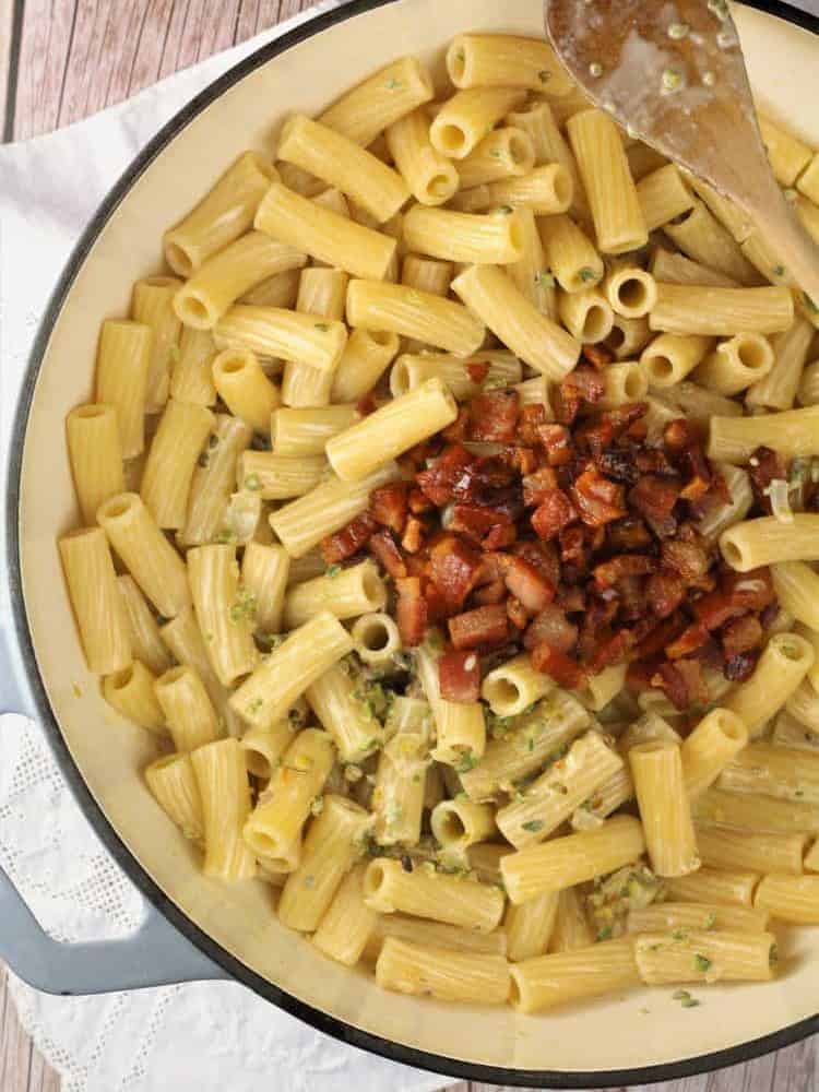 Pistachio pasta topped with sautéed pancetta in skillet.