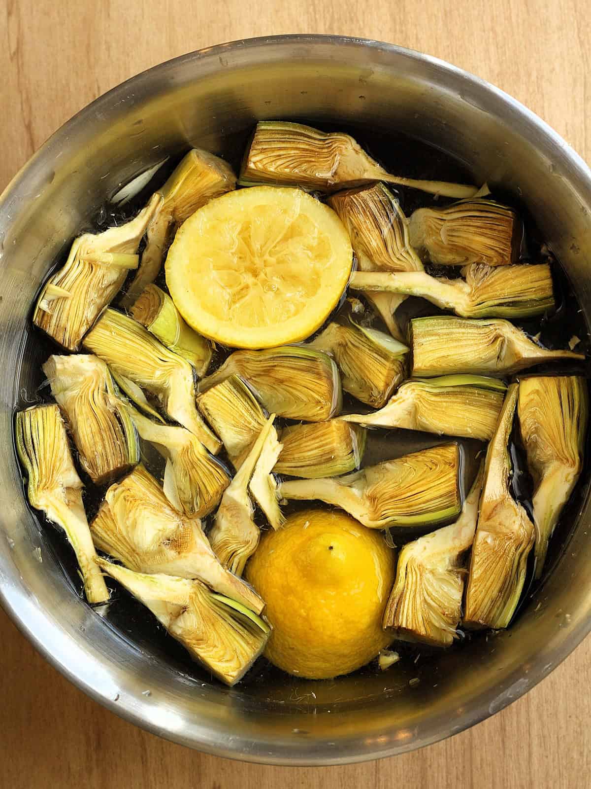 Cleaned artichoke quarters in bowl with lemon halves.