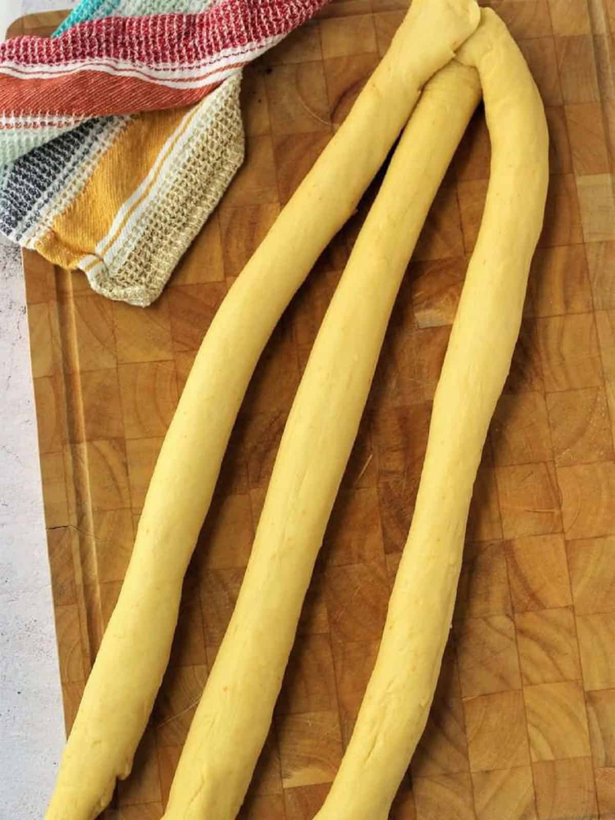 Brioche dough divided into 3 ropes with one end pinched together for braiding.