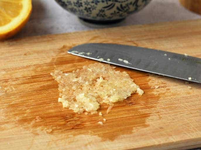 Garlic paste on wood board with knife for aioli.