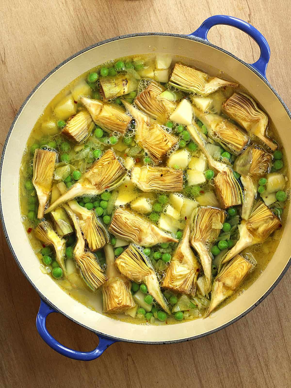 Artichoke quarters, peas and potatoes in large skillet submerged in water.