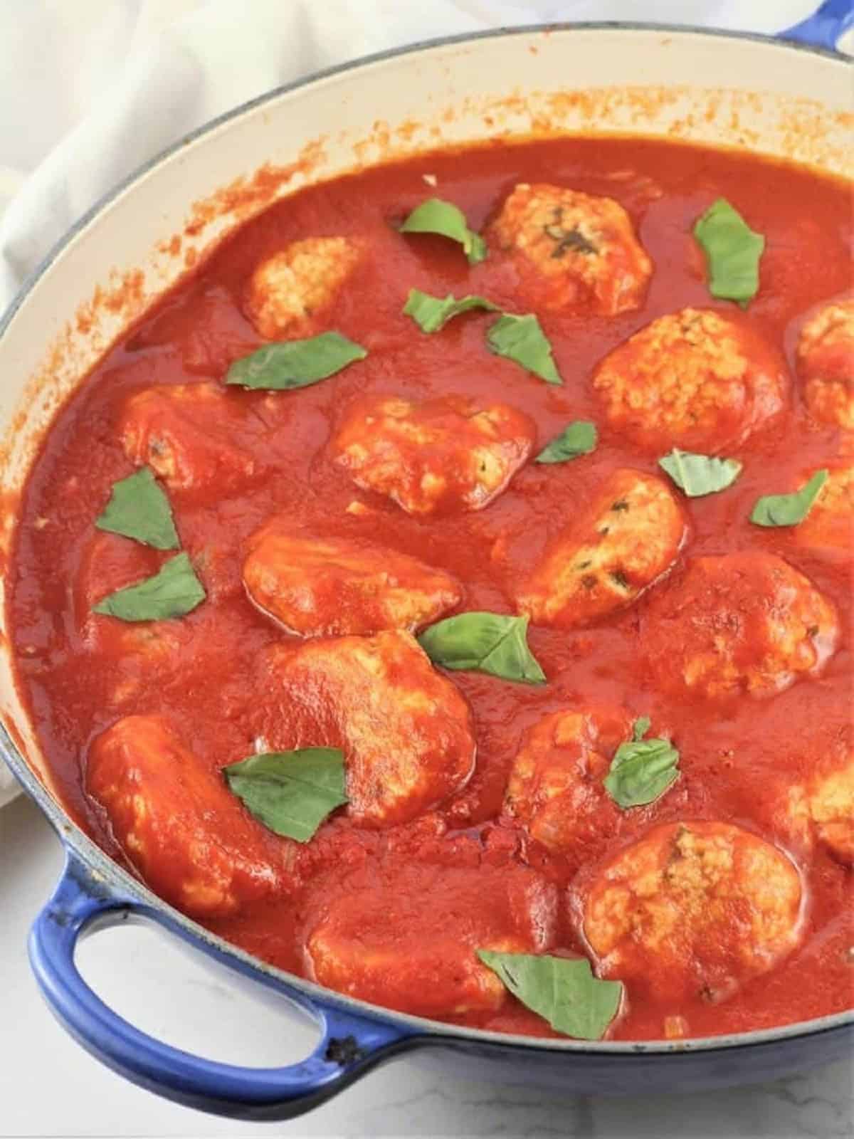 Italian vegetarian meatballs simmering in tomato sauce, topped with basil leaves.