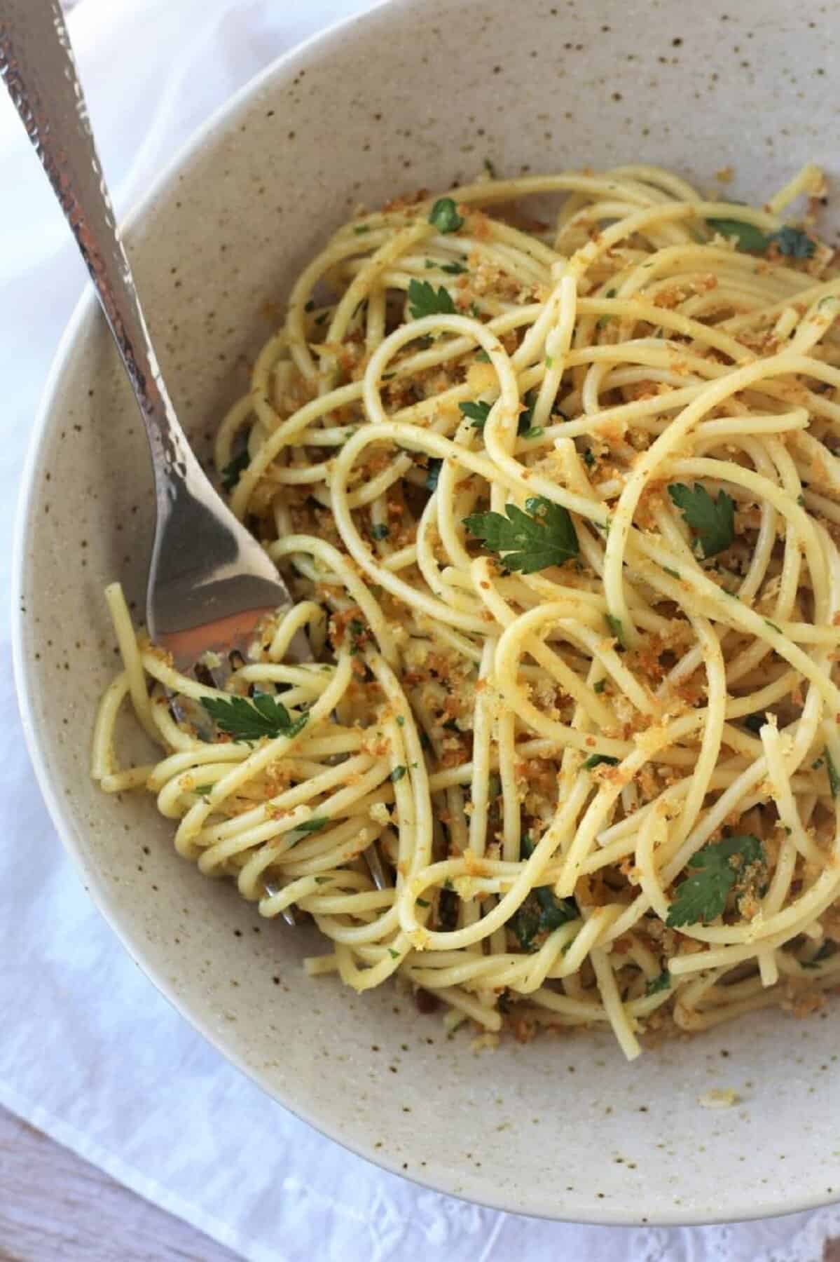 Bowl of pasta with anchovies and breadcrumbs with fork in it.