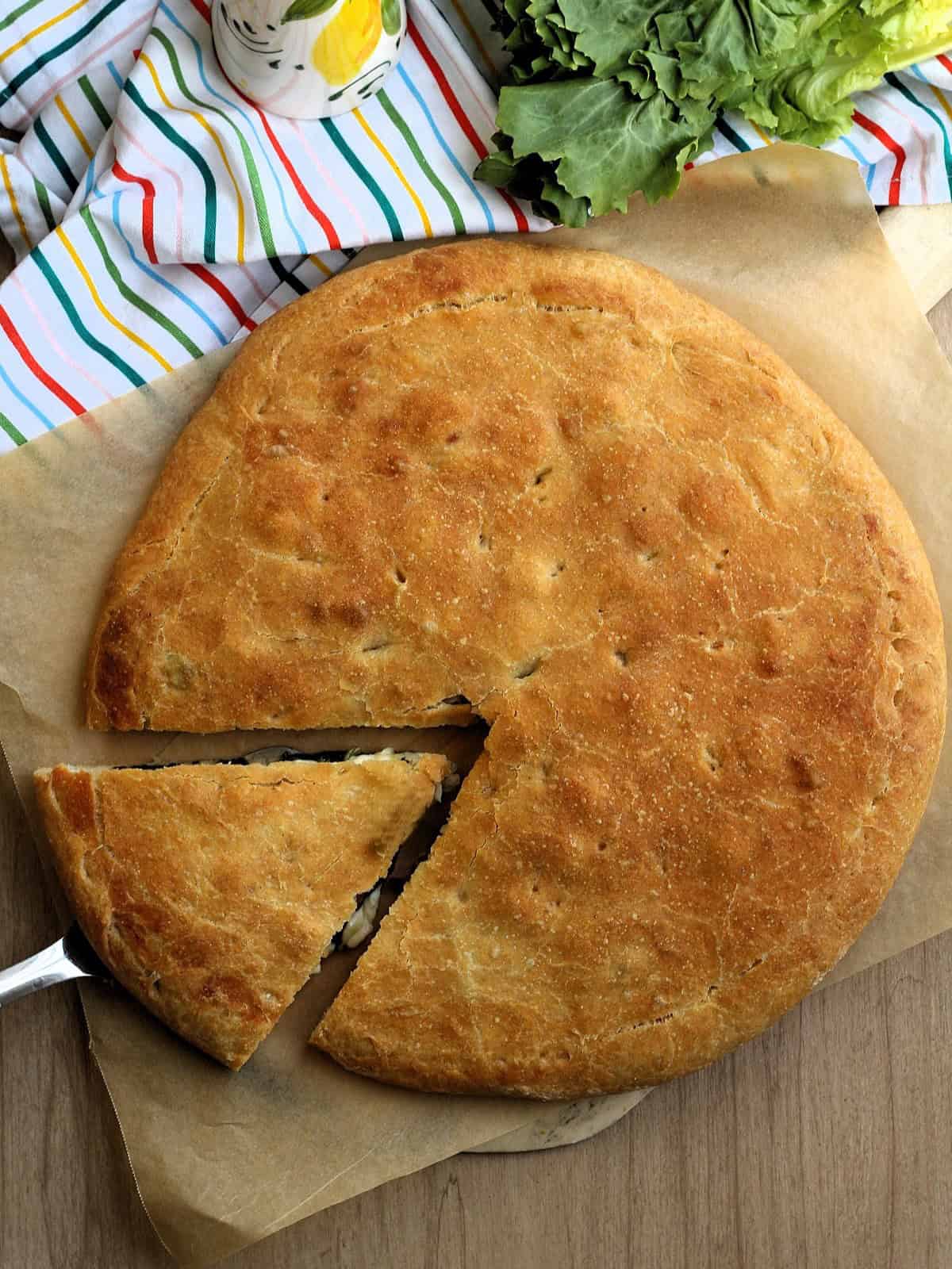 Sicilian scacciata Messinese on wood board with wedge cut out.