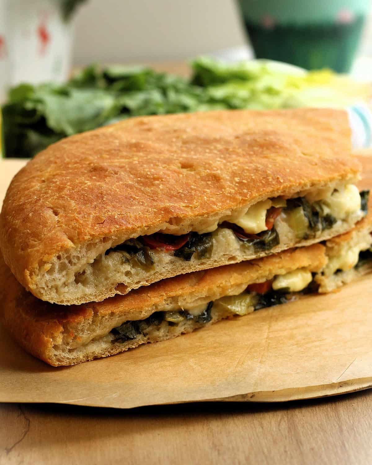 Sicilian stuffed focaccia recipe with escarole cut in half on wood board.