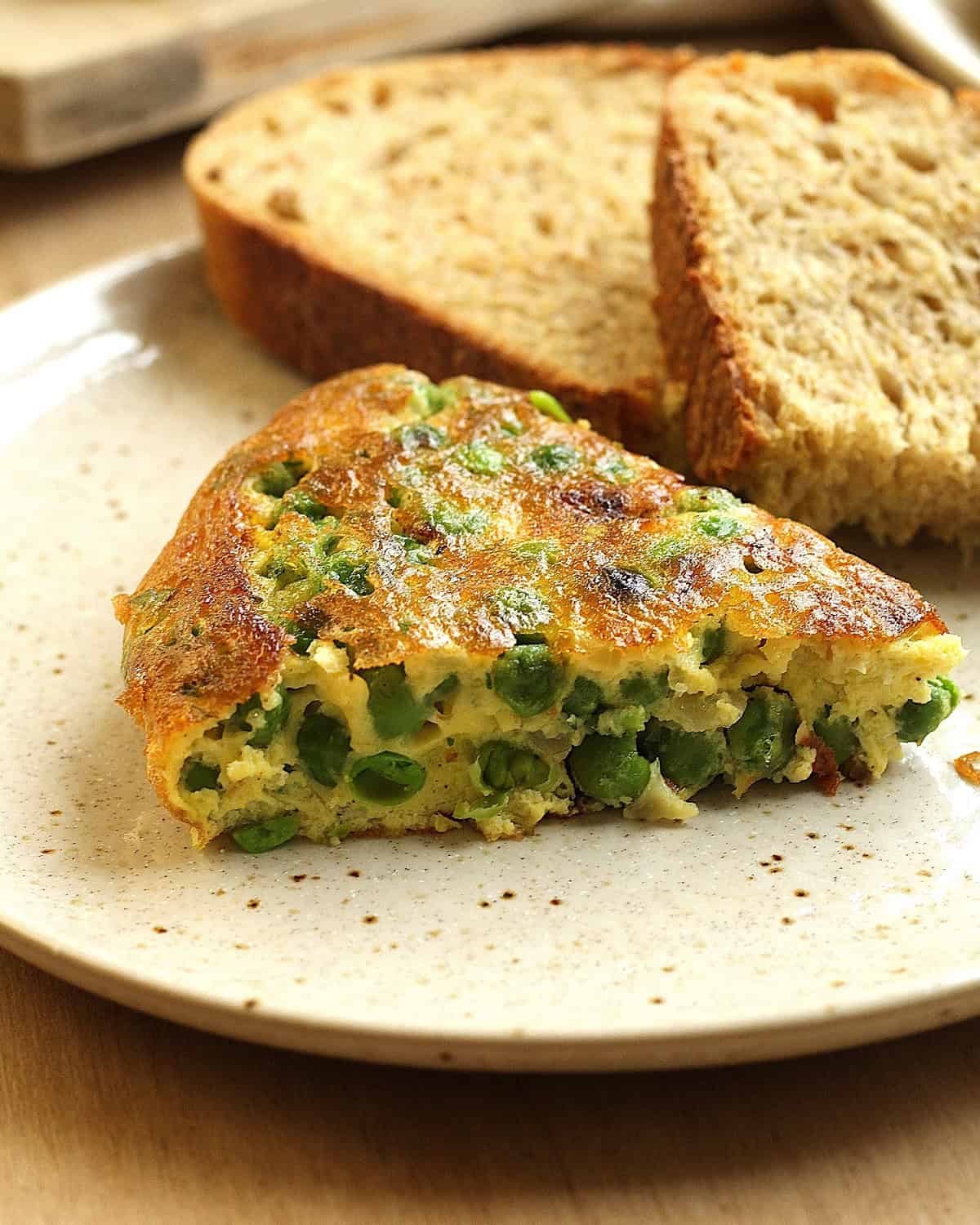 Slice of Italian baked frittata with peas next to bread.