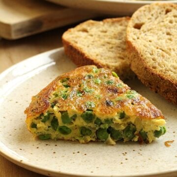 Wedge of baked frittata with peas on plate with slices of bread.