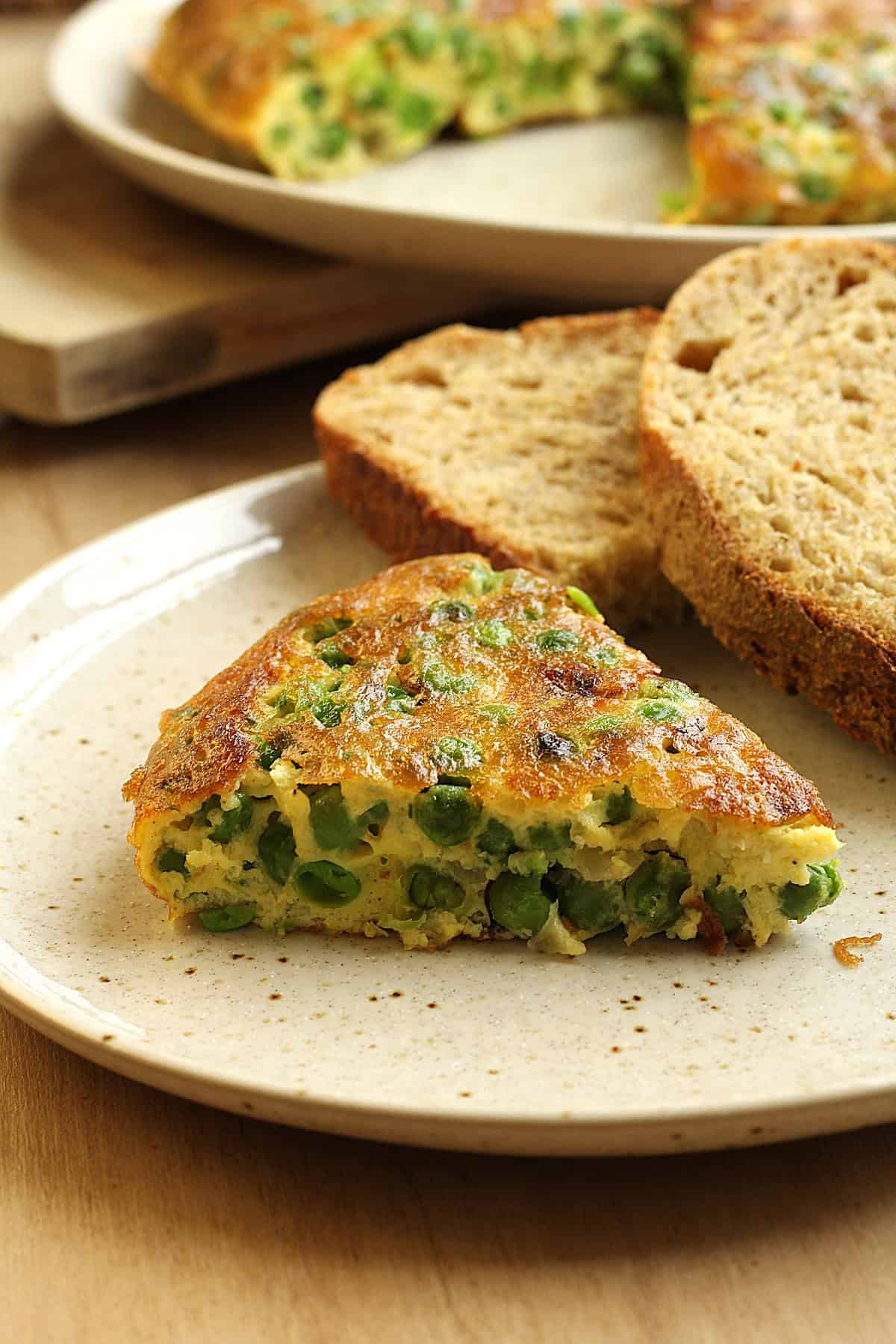 Wedge of baked frittata with peas on plate with slices of bread.