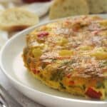 Potato frittata with red peppers on plate surrounded by bread slices.