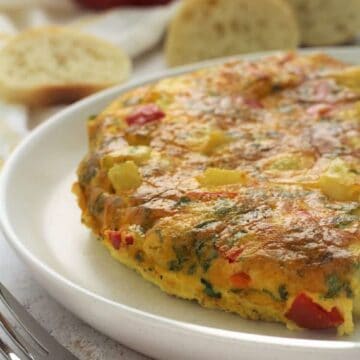 Potato frittata with red peppers on plate surrounded by bread slices.