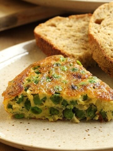 Slice of frittata with peas next to sliced bread.