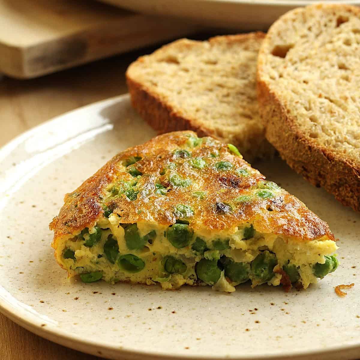 Slice of frittata with peas next to sliced bread.