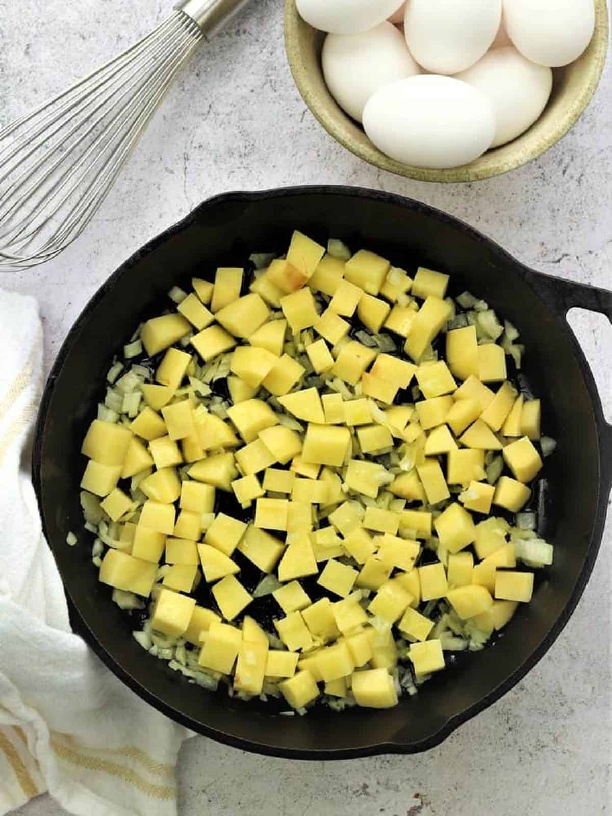 Cubed potatoes and diced onion sautéed in skillet for frittata recipe.