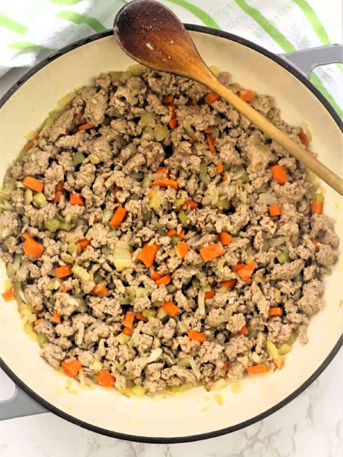 Ground meat added to skillet with diced vegetables for meat sauce.