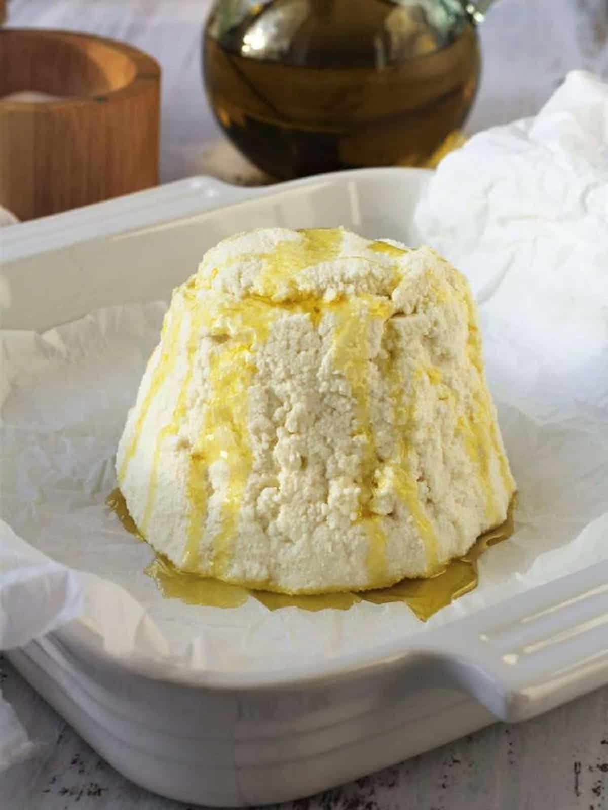 Whole ricotta drizzled with olive oil and salt on baking dish.