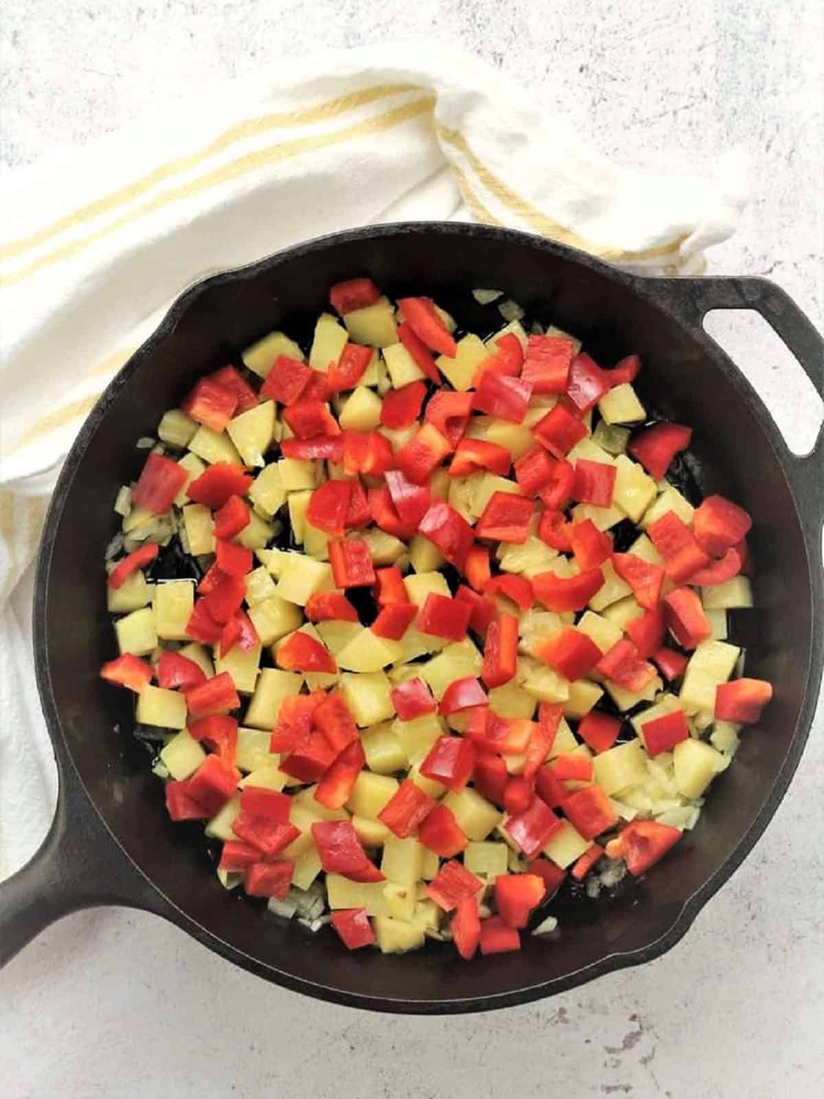 Sautéed potato and red peppers in skillet for frittata recipe.