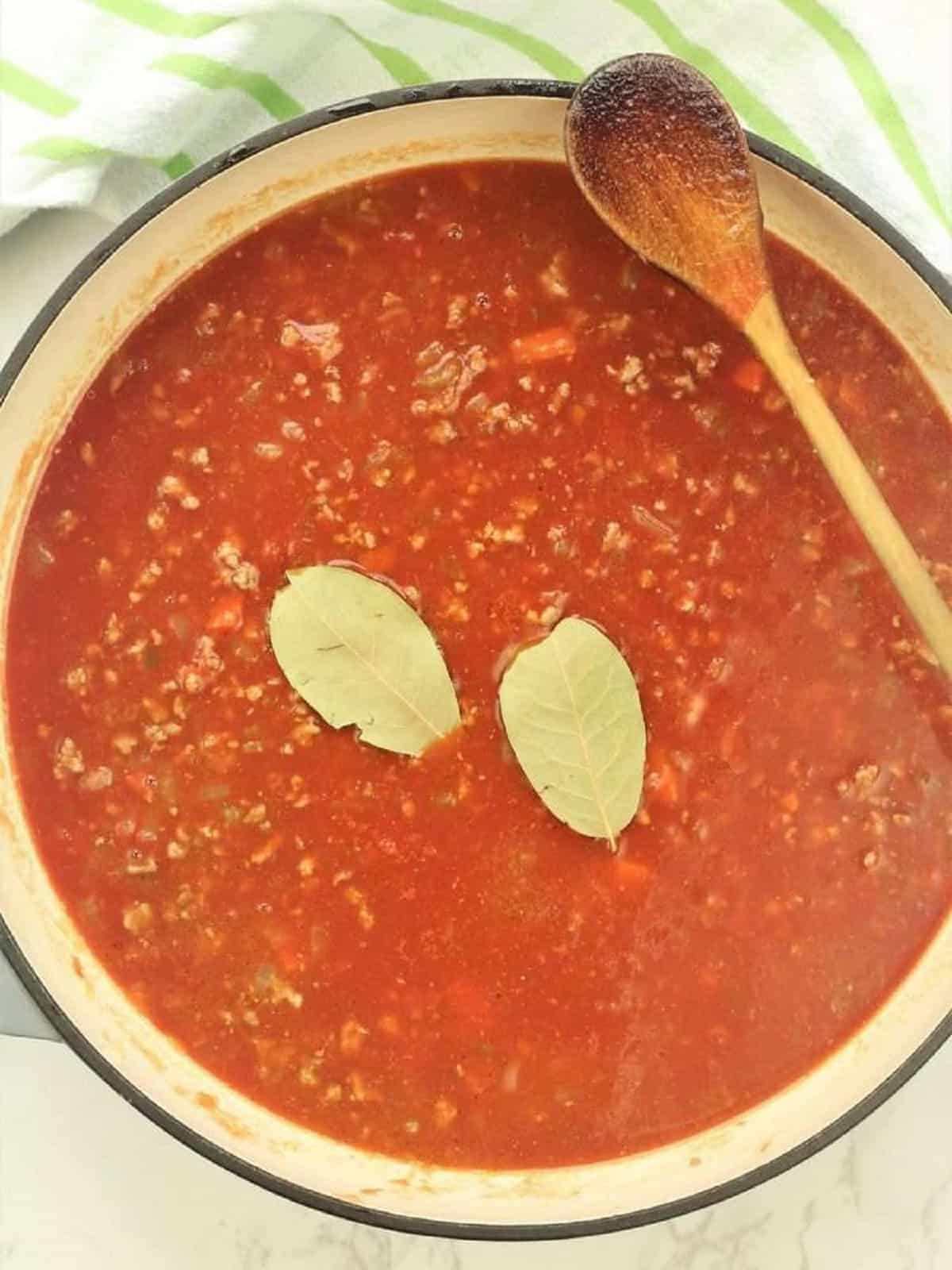 Meat tomato sauce in skillet with bay leaves added.